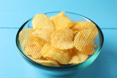 Lezzetli patates cipsleri mavi ahşap masada, yakın plan.