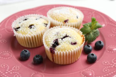 Yaban mersinli lezzetli kekler, pudra şekeri ve nane şekeri beyaz masada, yakın plan.