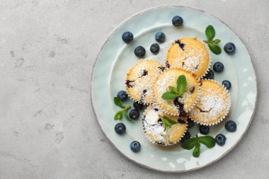 Yaban mersinli lezzetli kekler, pudra şekeri ve gri desenli masada nane şekeri, üst manzara. Metin için boşluk