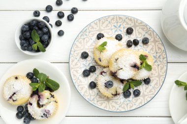 Yaban mersinli leziz çörekler, pudra şekeri ve beyaz ahşap masa üzerinde nane şekeri.