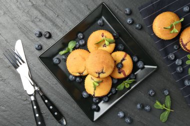 Yaban mersinli lezzetli kekler, nane ve çatal bıçak seti koyu dokulu masa, düz uzanmış.