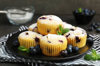 Yaban mersinli lezzetli çörekler, pudra şekeri ve nane şekeri siyah masada, yakın plan.