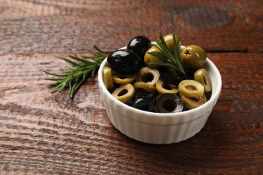 Farklı lezzetlerde marine edilmiş zeytin halkaları, hepsi ve biberiye ahşap masada, yakın plan.
