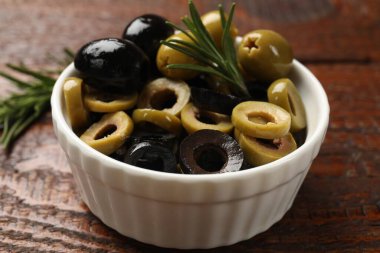 Farklı lezzetlerde marine edilmiş zeytin halkaları, hepsi ve biberiye ahşap masada, yakın plan.
