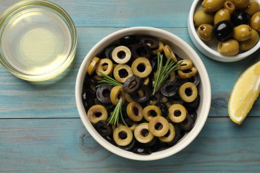 Farklı lezzetli marine edilmiş zeytin halkaları, bütün olanlar, biberiye ve yağ açık mavi ahşap masa, düz uzanmış