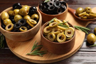 Farklı lezzetlerde marine edilmiş zeytin halkaları, tüm olanlar ve ahşap masada biberiye, yakın plan.