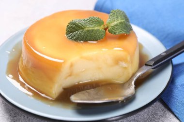 Karamel soslu lezzetli puding, gri desenli masada nane ve kaşık, yakın plan.