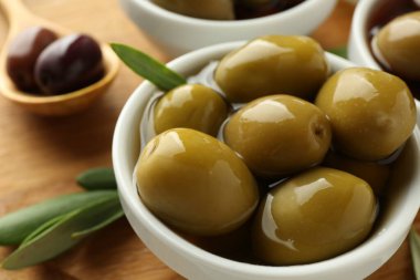 Lezzetli marine edilmiş zeytinler kasede, kaşık ve yeşil yapraklar masada, yakın plan