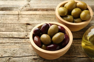 Lezzetli marine edilmiş zeytinler kaselerde ve ahşap masada yağ, yakın plan. Metin için boşluk