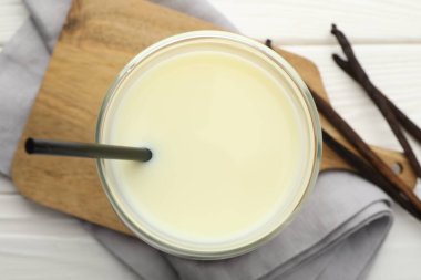 Bardakta vanilyalı süt ve beyaz ahşap masada kapsüller.