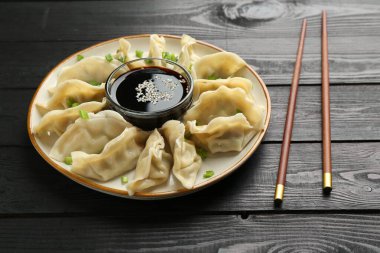 Lezzetli haşlanmış gyoza (hamur tatlısı) ve siyah ahşap masada servis edilen yeşil soğan.