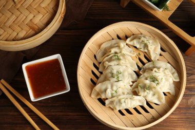 Bambu buharlı buharda kaynamış gyoza (hamur tatlısı), sos ve çubuklar ahşap masada, düz yerde.