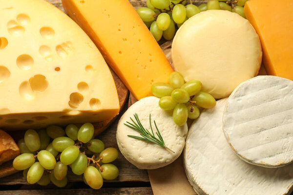 Different types of cheese, rosemary and grapes on wooden table, flat lay