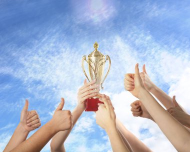 Altın kupa tutan kadın ve gökyüzüne başparmak gösteren insanlar, yakın plan.