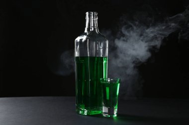Siyah arkaplanda dumanlı Absinthe bardakta ve şişede