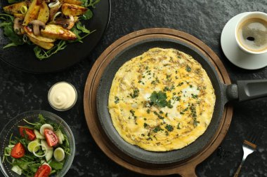 Lezzetli bir kahvaltı. Lezzetli omlet, salata, kızarmış patates ve siyah desenli masada servis edilen kahve.