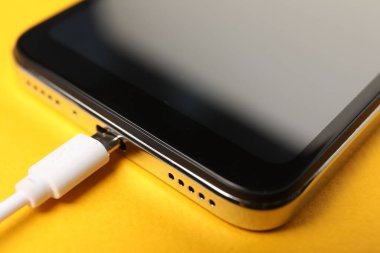 USB şarj kablosu turuncu arka plandaki akıllı telefona bağlı, yakın plan