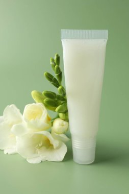 Açık yeşil arka planda dudak kremi ve frezya çiçekleri, yakın plan.