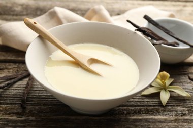 Lezzetli yoğunlaştırılmış süt, kaşık, vanilya kabukları ve çiçek ahşap masada, yakın plan.