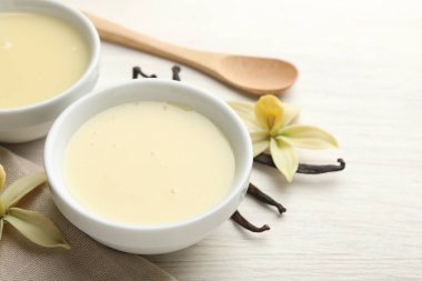 Lezzetli konsantre süt, vanilya kabukları, çiçekler ve kaşık beyaz ahşap masa, yakın plan