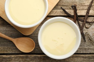 Yoğun süt, kaşık ve vanilya kapsülleri ahşap masada, düz yerde.