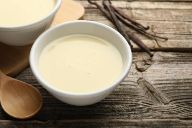 Tahta masadaki lezzetli konsantre süt, kaşık ve vanilya kapsülleri, yakın plan.