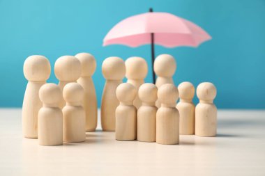 Şemsiye altındaki insan figürleri açık mavi arka plana karşı beyaz masada. Sigorta konsepti