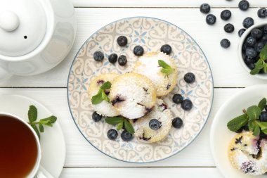 Yaban mersinli leziz çörekler, pudra şekeri ve beyaz ahşap masa üzerinde nane şekeri.