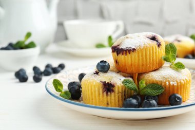 Yaban mersinli lezzetli kekler, pudra şekeri ve beyaz ahşap masada nane şekeri, yakın plan.