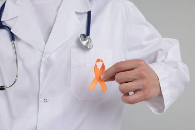 Çoklu Skleroz farkındalığı. Açık gri arka planda turuncu kurdeleli doktor, yakın plan.