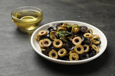 Farklı lezzetlerde marine edilmiş zeytin halkaları ve koyu dokulu masa üzerindeki yağ, yakın plan.