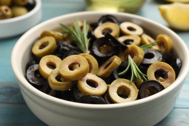 Farklı lezzetlerde marine edilmiş zeytin halkaları ve biberiye açık mavi ahşap masada, yakın plan.