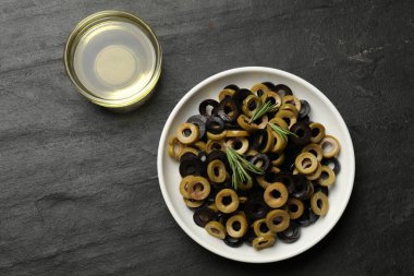 Farklı lezzetlerde marine edilmiş zeytin halkaları, biberiye ve yağ koyu dokulu masa, düz uzanış