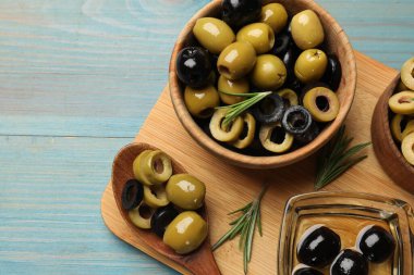 Farklı lezzetlerde marine edilmiş zeytin halkaları, tüm olanlar ve açık mavi ahşap masa üzerinde biberiye, üst manzara. Metin için boşluk