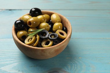 Farklı lezzetlerde marine edilmiş zeytin halkaları ve açık mavi ahşap masada biberiye, yakın plan. Metin için boşluk