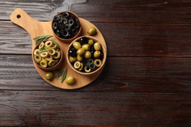 Farklı lezzetlerde marine edilmiş zeytin halkaları, tüm olanlar ve ahşap masa üzerinde biberiye, üst manzara. Metin için boşluk