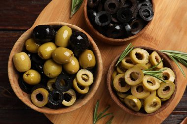 Farklı lezzetlerde marine edilmiş zeytin halkaları, tüm olanlar ve ahşap masa üzerinde biberiye, üst manzara