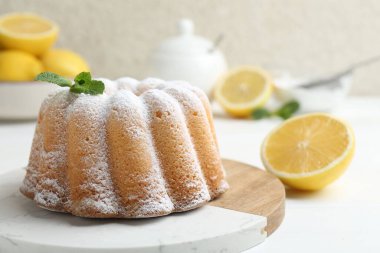 Beyaz ahşap masada pudra şekerli, nane ve narenciye meyveli lezzetli limonlu pasta, yakın plan.