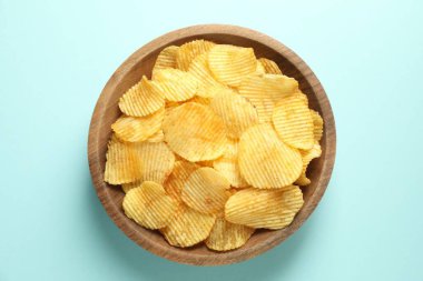 Açık mavi arka planda kasede patates cipsi, üst manzara.