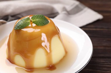 Karamel soslu lezzetli puding ve ahşap masada nane şekeri, yakın plan.