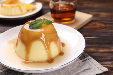 Karamel soslu lezzetli puding ve ahşap masada nane şekeri, yakın plan.
