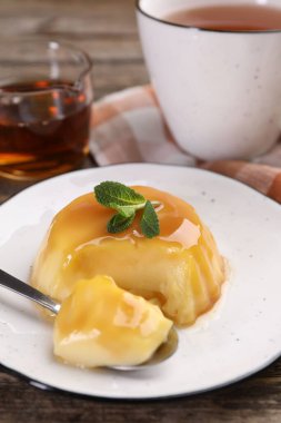 Karamel soslu lezzetli puding ve ahşap masada servis edilen nane, yakın plan.