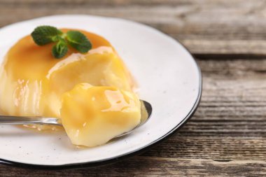 Karamel soslu lezzetli puding ve ahşap masada servis edilen nane, yakın plan.