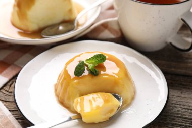 Karamel soslu lezzetli puding ve ahşap masada servis edilen nane, yakın plan.