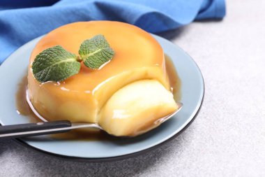 Karamel soslu lezzetli puding, gri desenli masada nane ve kaşık, yakın plan. Metin için boşluk