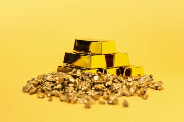 Sarı arkaplanda altın külçeler ve çubuklar, yakın plan.