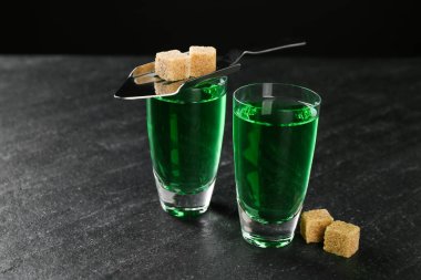 Absinthe shot bardakları, esmer şeker ve siyah masanın üzerine konmuş kaşık, yakın plan.