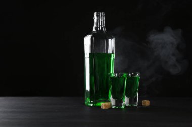 Absinthe shot bardakları, şişe ve esmer şeker siyah arka planda duman, mesaj için boşluk
