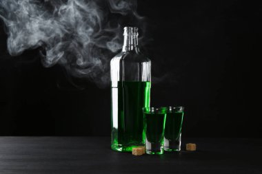 Absinthe shot bardakları, şişe ve esmer şeker siyah arka planda dumanlı