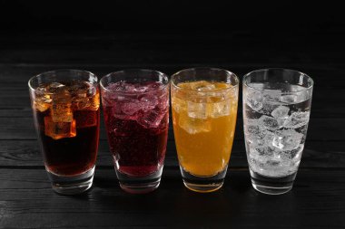 Farklı aromalı soda ve siyah ahşap masada buz küpleri.